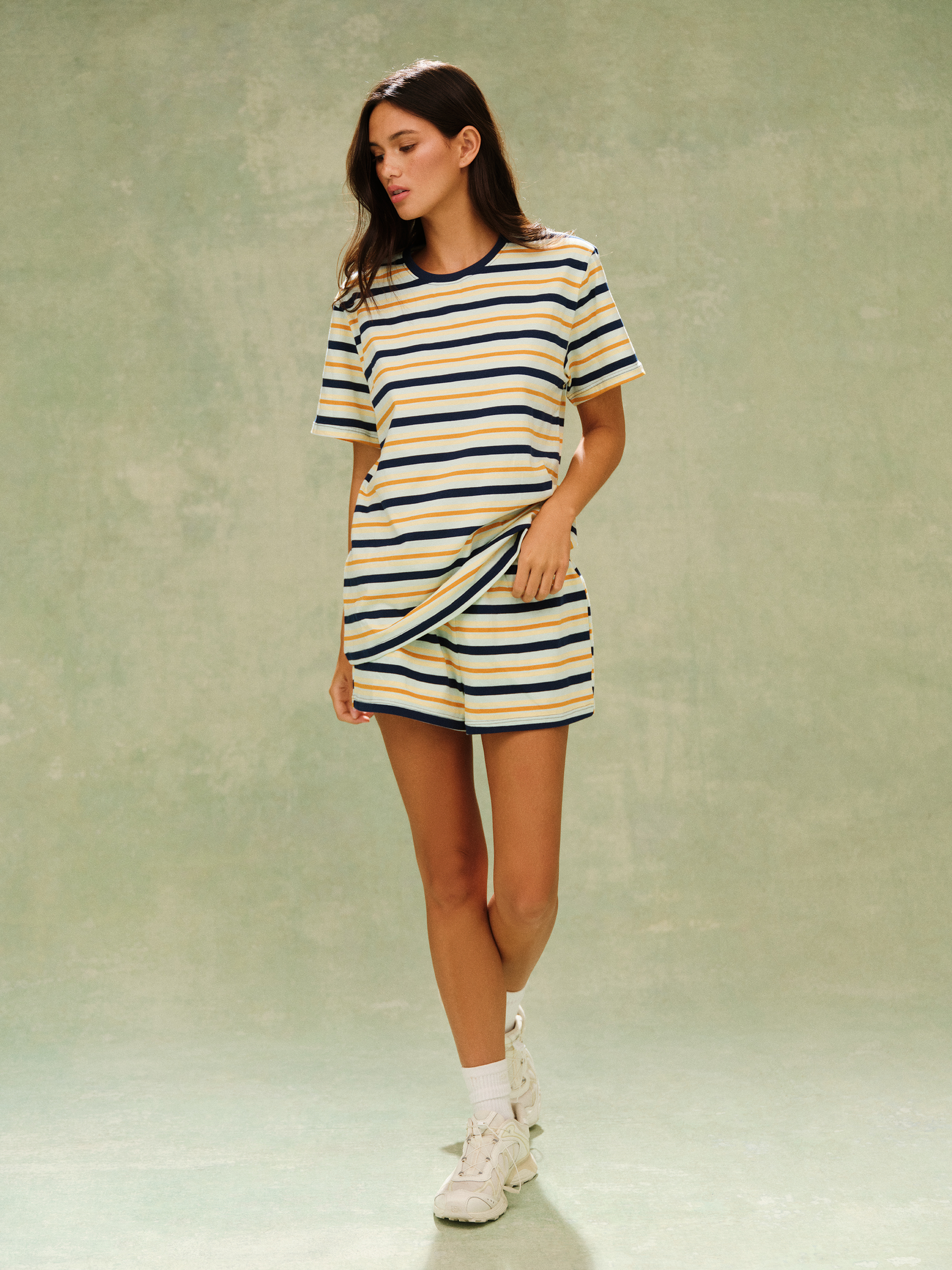 Woman wearing a striped dress with white sneakers on a plain background