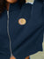 Navy blue jacket with a gold embroidered logo on a neutral background