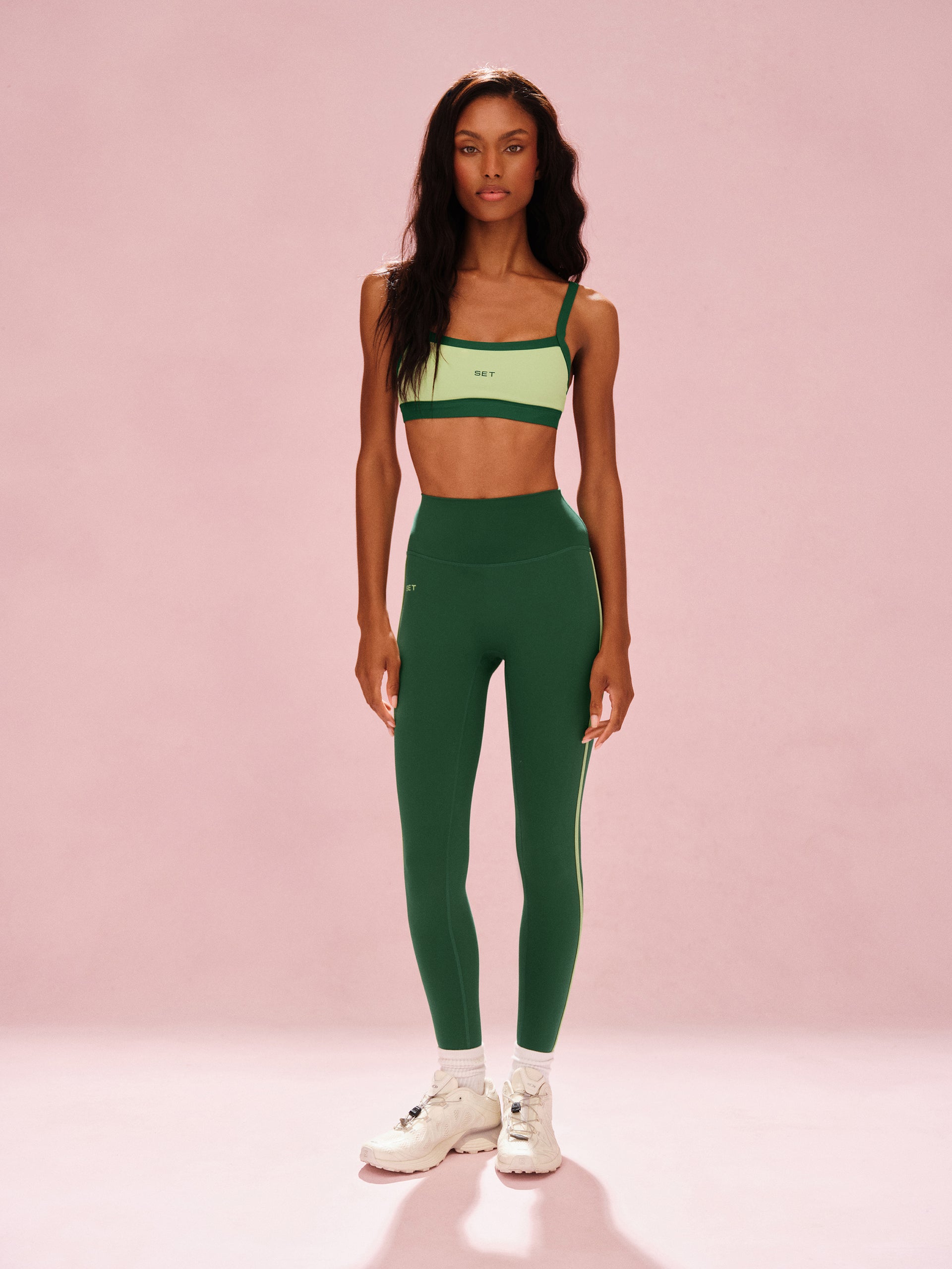 Woman wearing a green sports bra and leggings set on a pink background