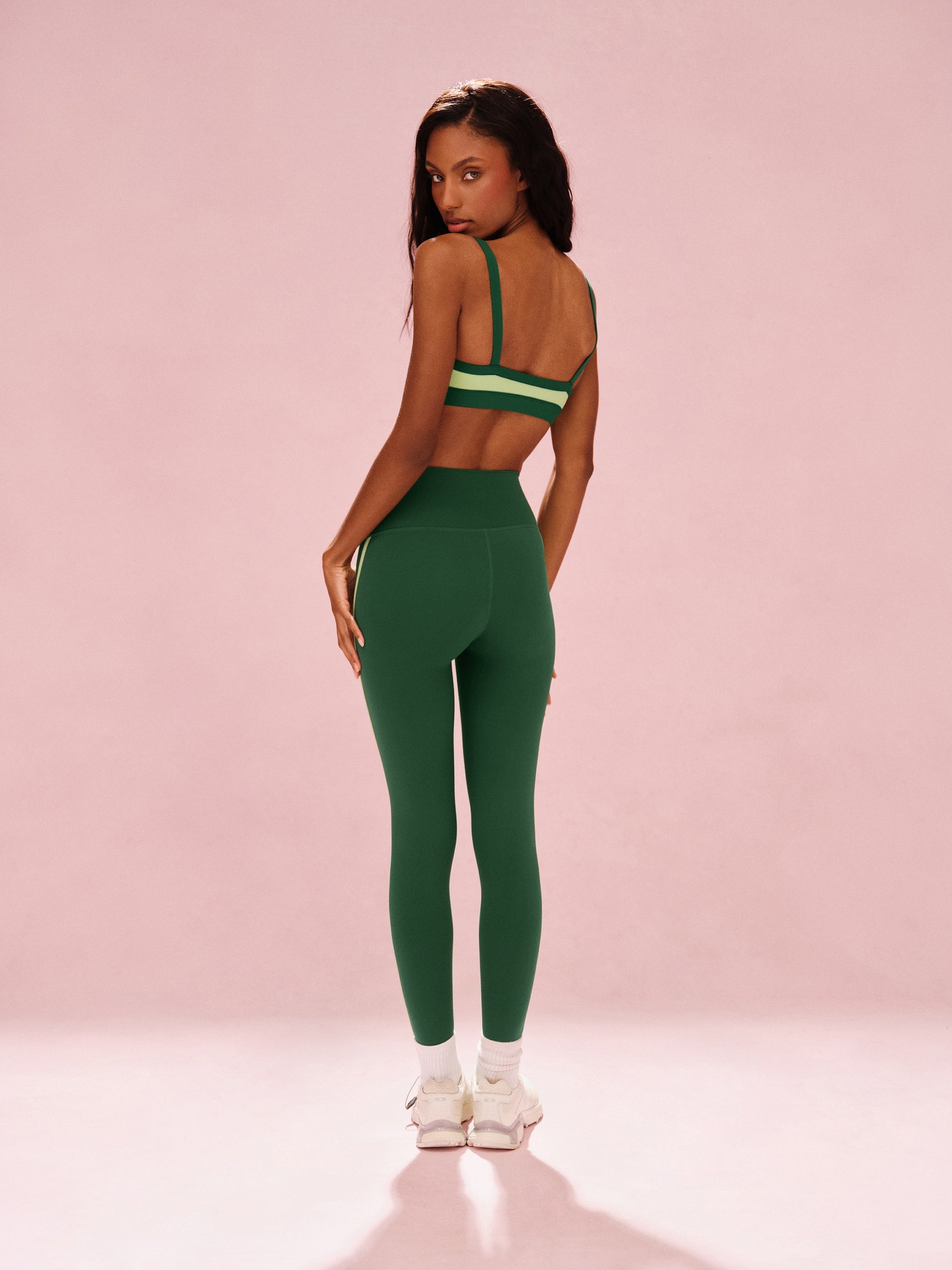 Woman wearing a green sports bra and leggings set on a pink background