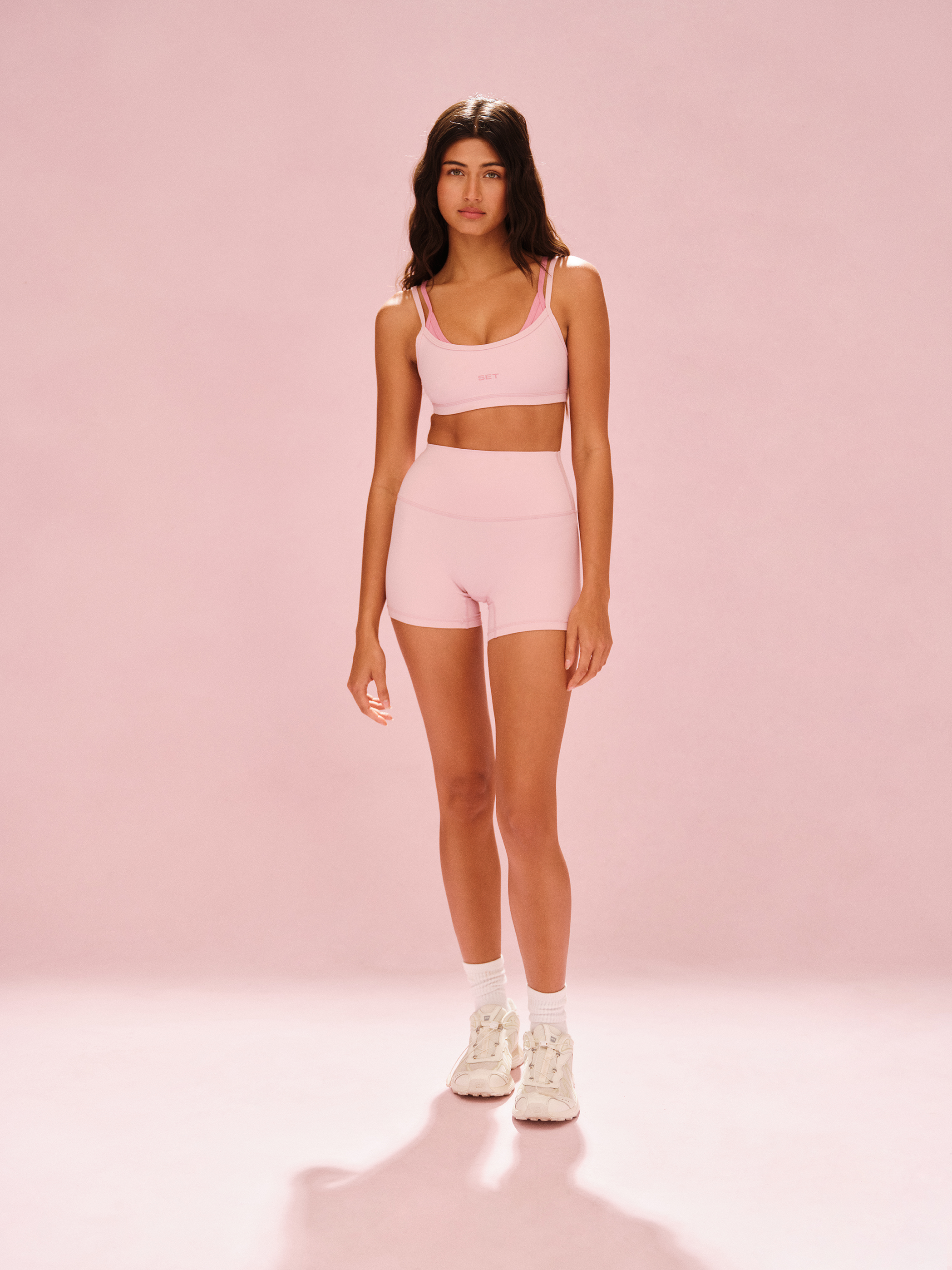 Woman wearing a pink sports bra and shorts set on a pink background