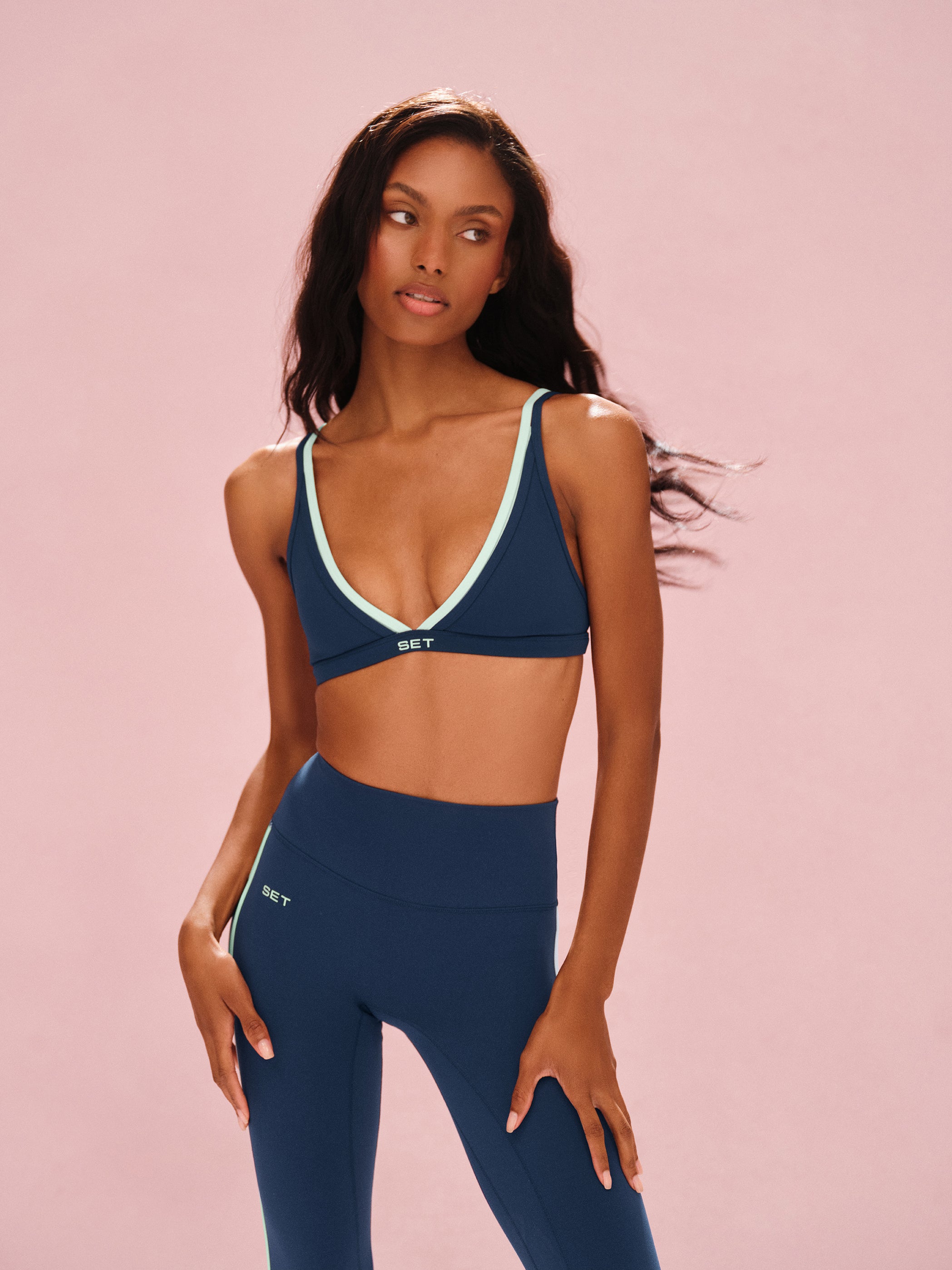 Woman wearing a navy sports bra and leggings set on a pink background