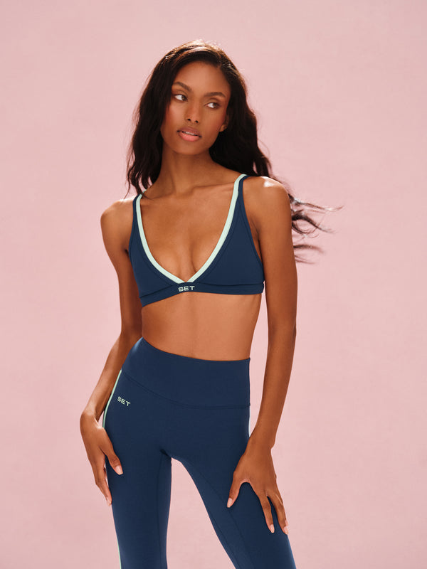 Woman wearing a navy sports bra and leggings set on a pink background