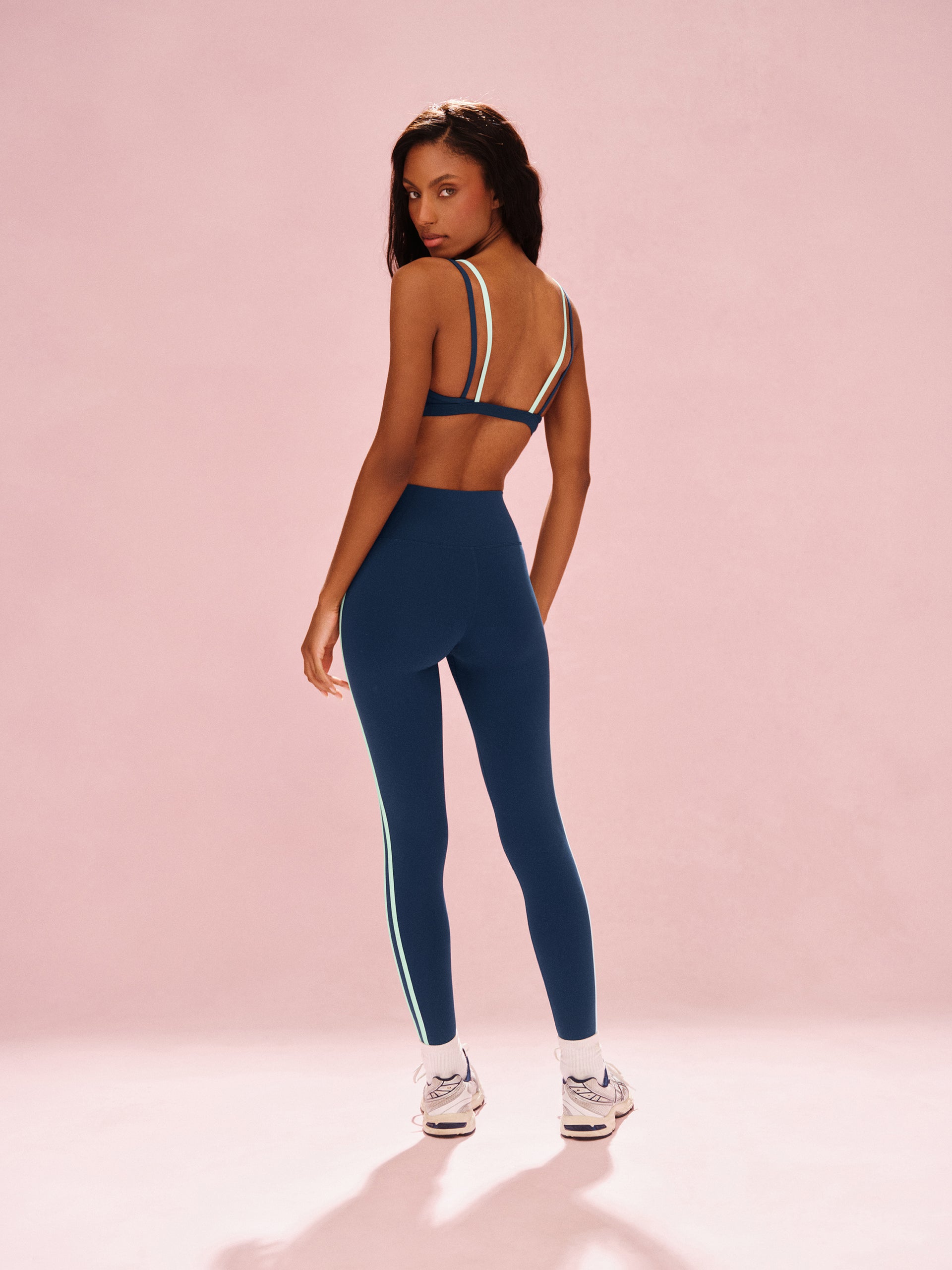 Woman wearing a blue athletic outfit with white stripes on a pink background