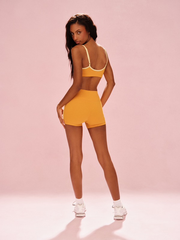 Woman wearing a yellow sports bra and shorts set on a pink background