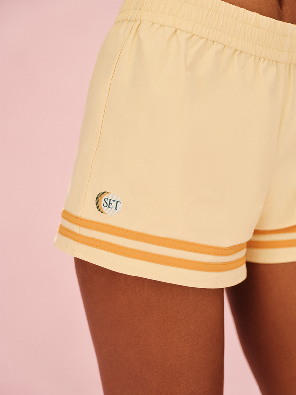 Yellow shorts with orange stripes and a logo on a pink background