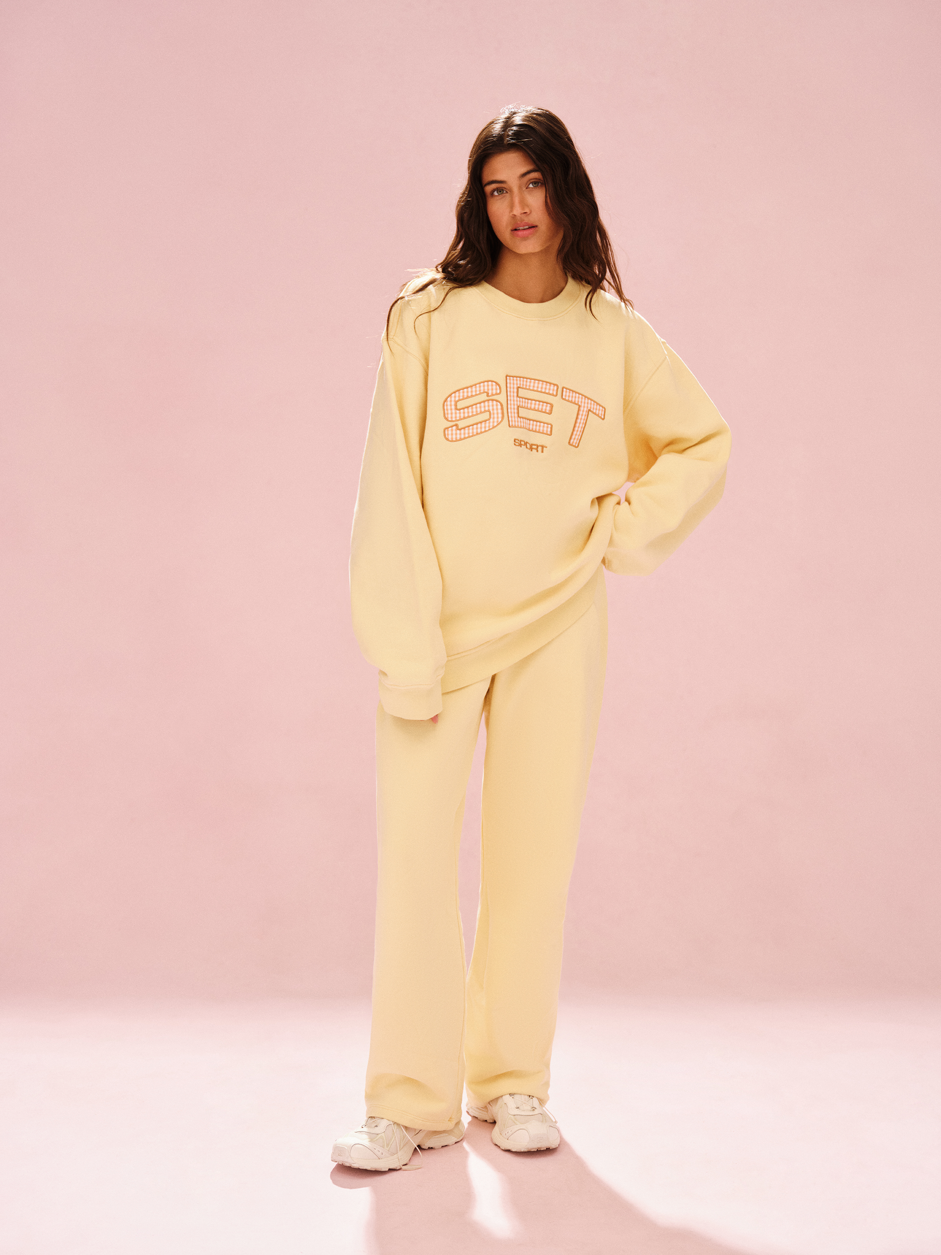 Woman wearing a yellow 'SET' sweatshirt and pants on a pink background