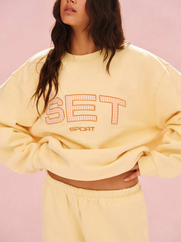 Person wearing a yellow sweatshirt with 'SET' printed on it against a pink background 