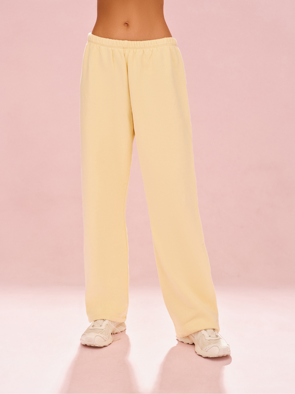Person wearing light yellow sweatpants on a pink background 