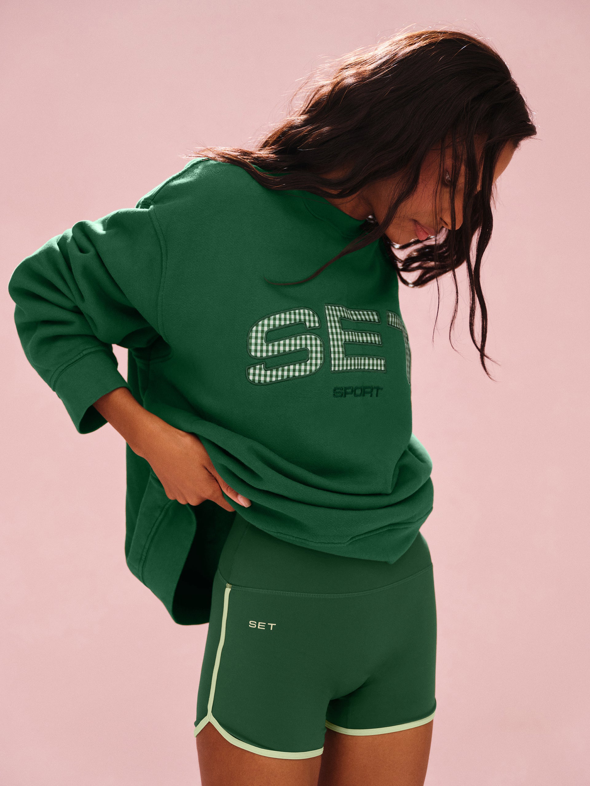 Person wearing a green 'SET' branded outfit on a pink background <model-info>Sydney wears a size M/L and is 5’9, 24½” waist, 32B bust.</model-info>