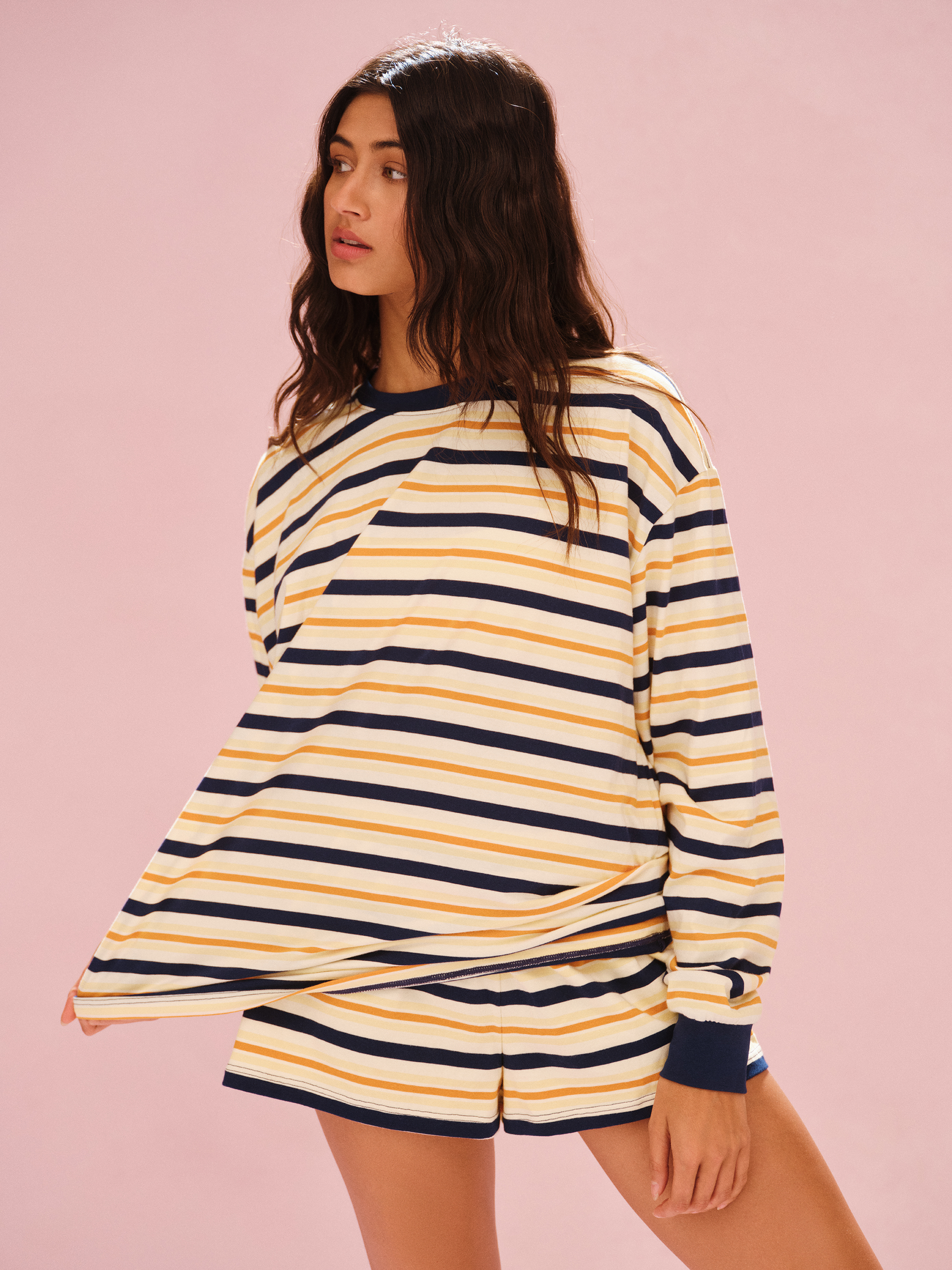 Woman wearing a yellow and navy striped long-sleeve shirt on a pink background