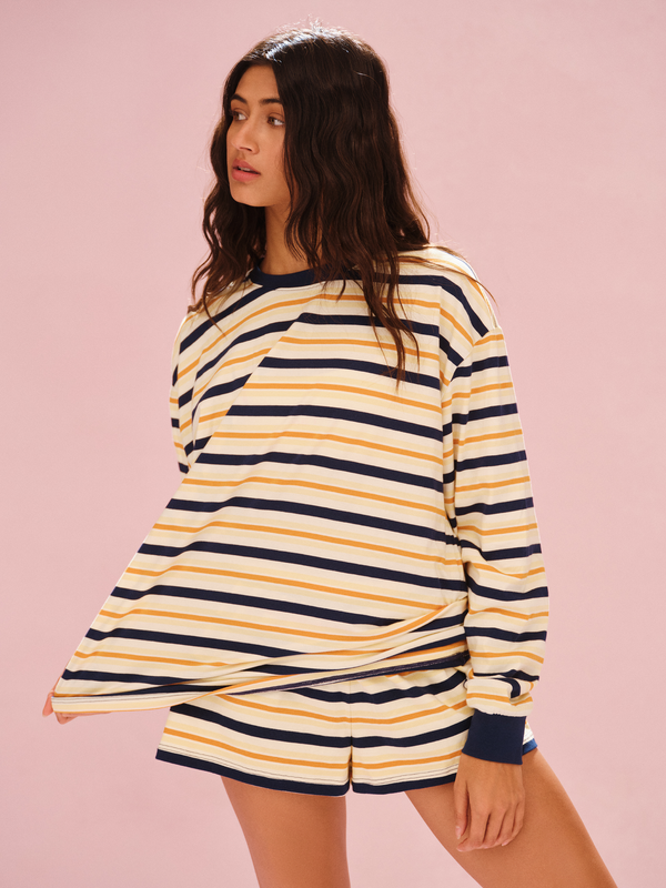 Woman wearing a yellow and navy striped long-sleeve shirt on a pink background