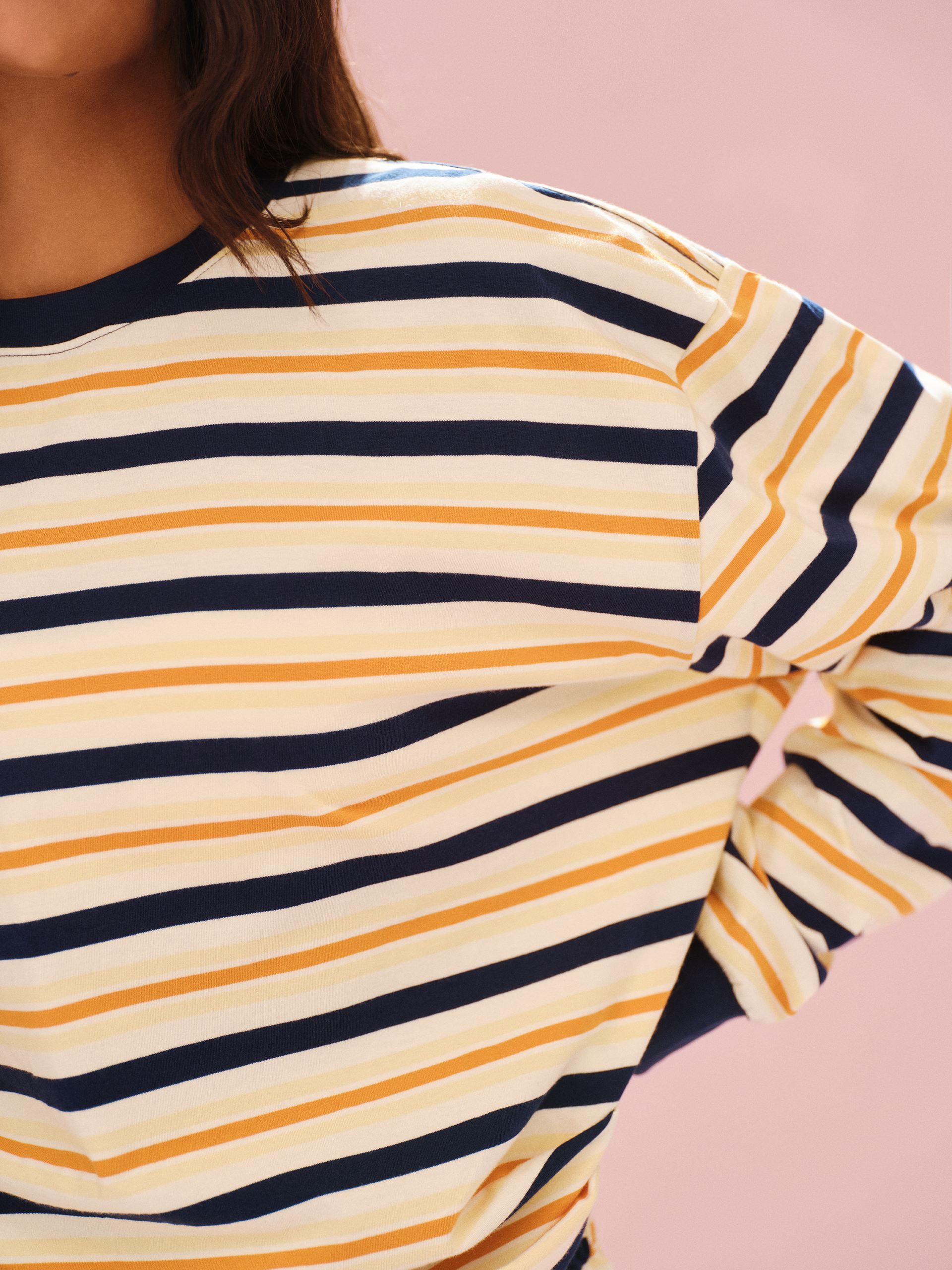 Close-up of a person wearing a striped shirt with yellow and navy horizontal stripes on a pink background.