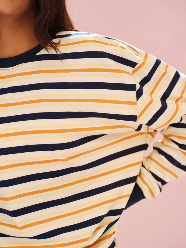 Close-up of a person wearing a striped shirt with yellow and navy horizontal stripes on a pink background.