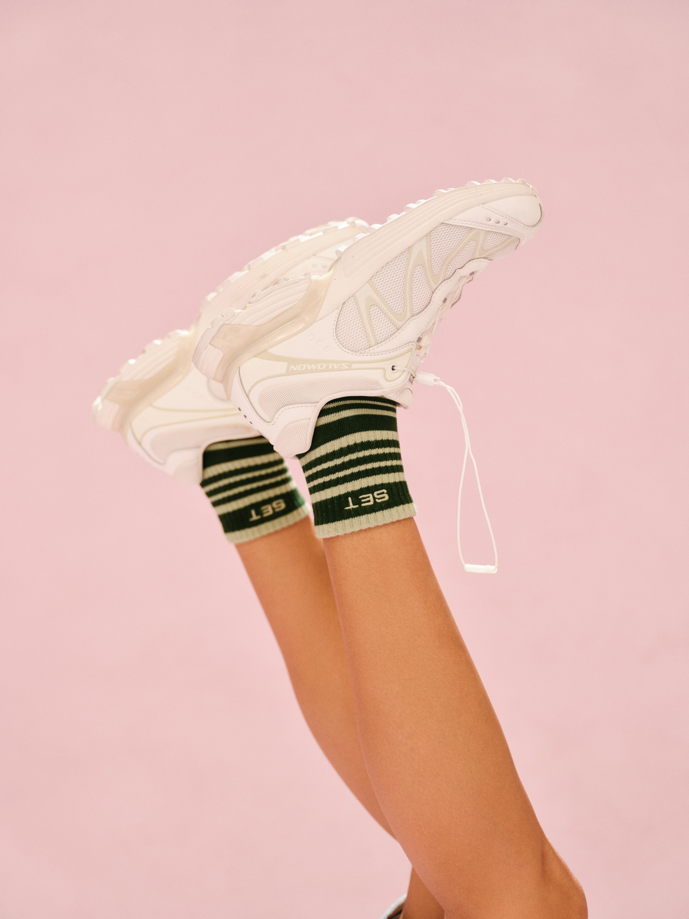 White sneakers with green striped socks on a pink background