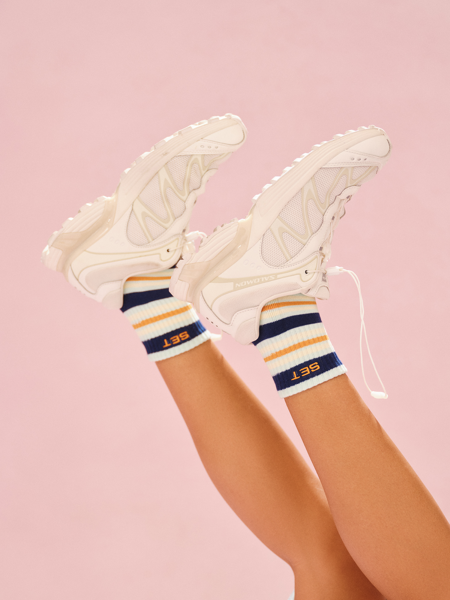 White sneakers with colorful striped socks on a pink background