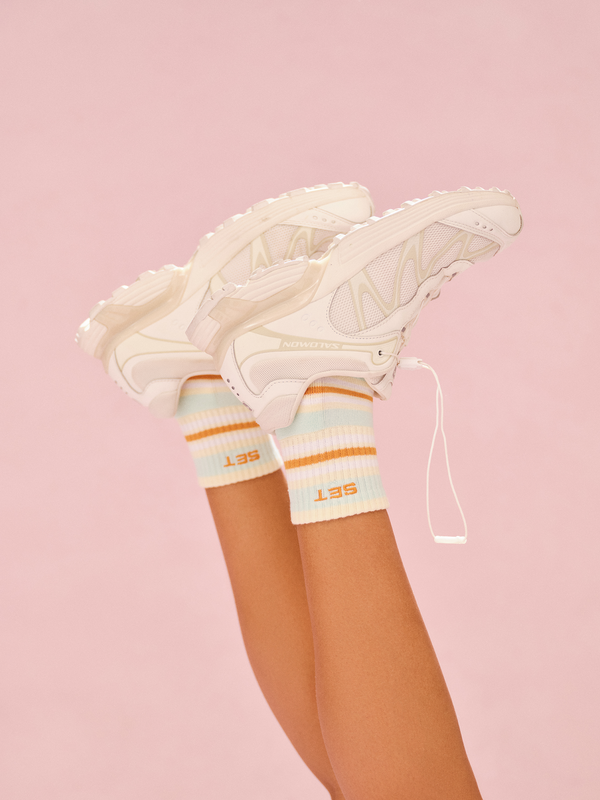White sneakers with colorful accents worn with striped knee-high socks on a pink background