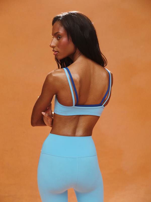 Woman wearing a blue sports bra and leggings against an orange background