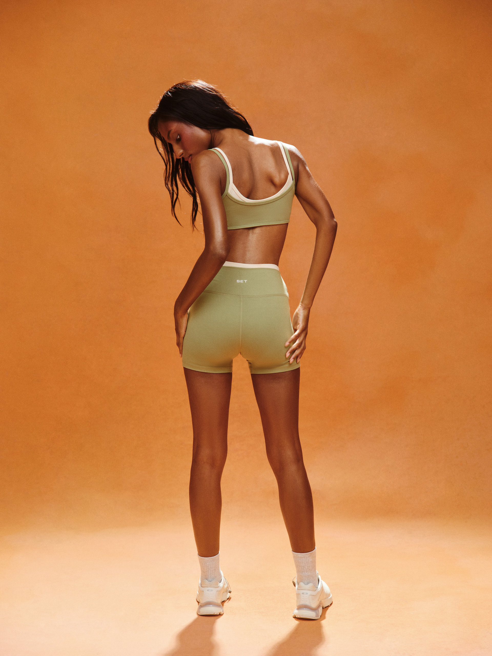 Woman wearing a green sports bra and shorts set on an orange background