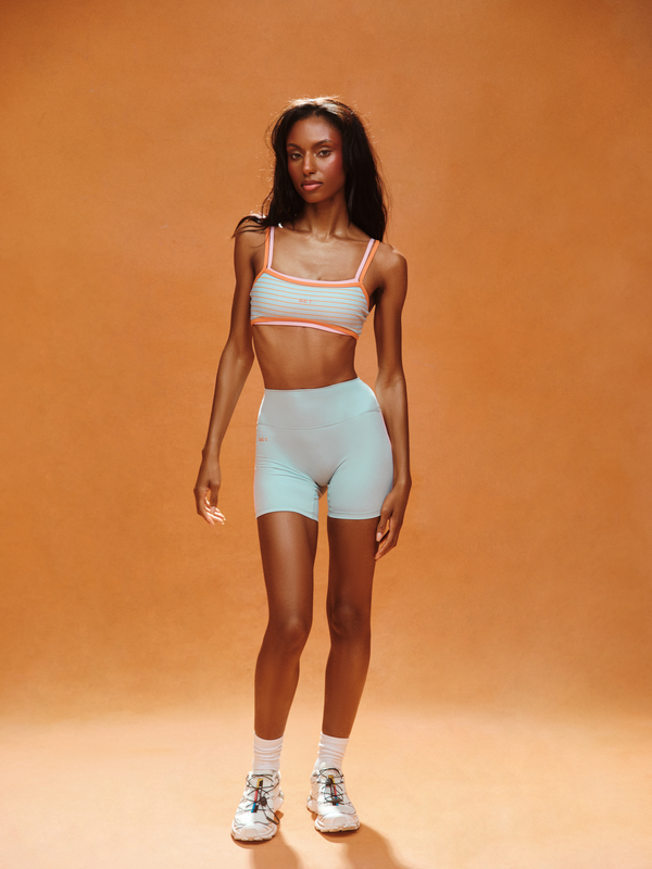 Woman wearing a light blue sports bra and shorts set on an orange background