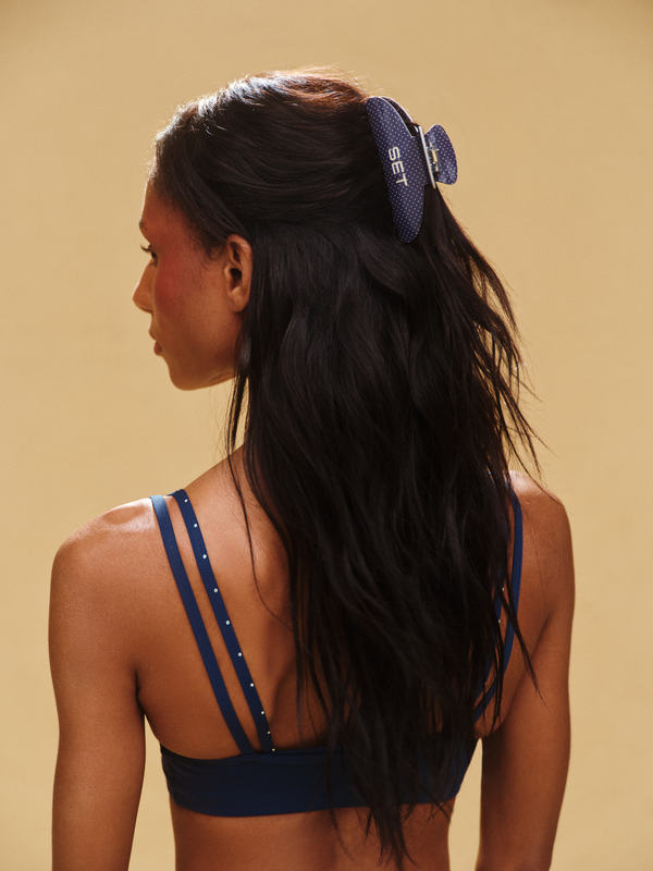 Woman wearing a blue sports bra with a claw clip on a beige background