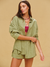 Woman wearing a green outfit with a beige background <model-info>Logan wears a size XS and is 5’9½”, 24” waist, 32B bust.</model-info>