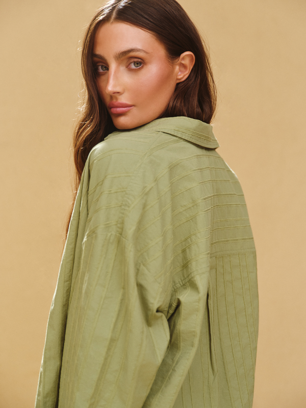 Woman wearing a green pleated shirt against a beige background