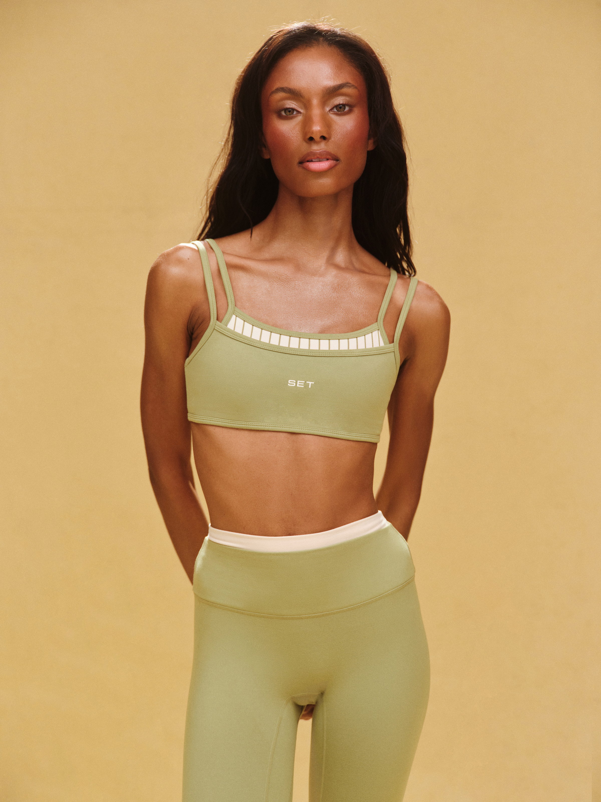 Woman wearing a green sports bra and leggings on a beige background 
