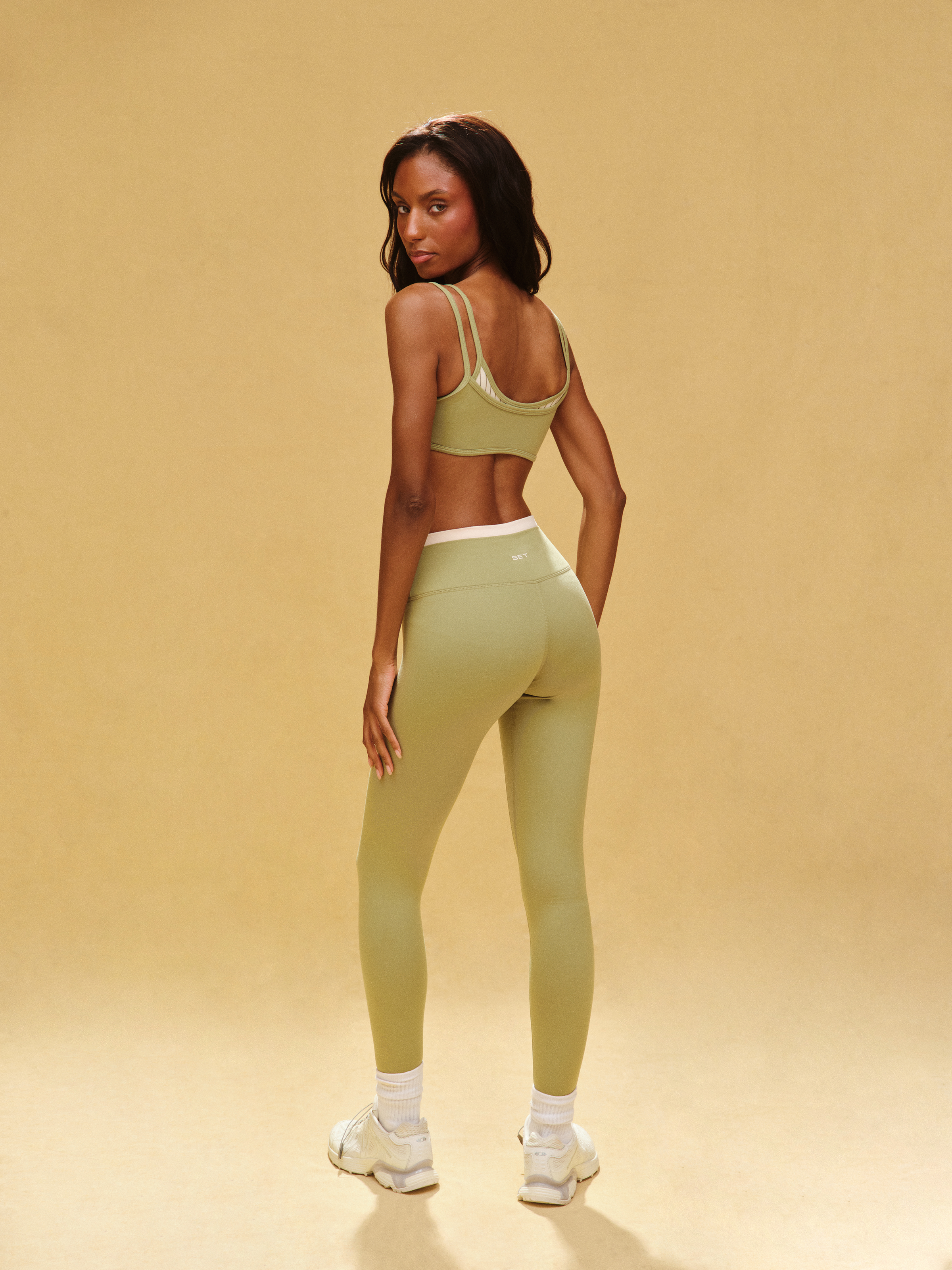 Woman wearing a green sports bra and leggings set on a beige background