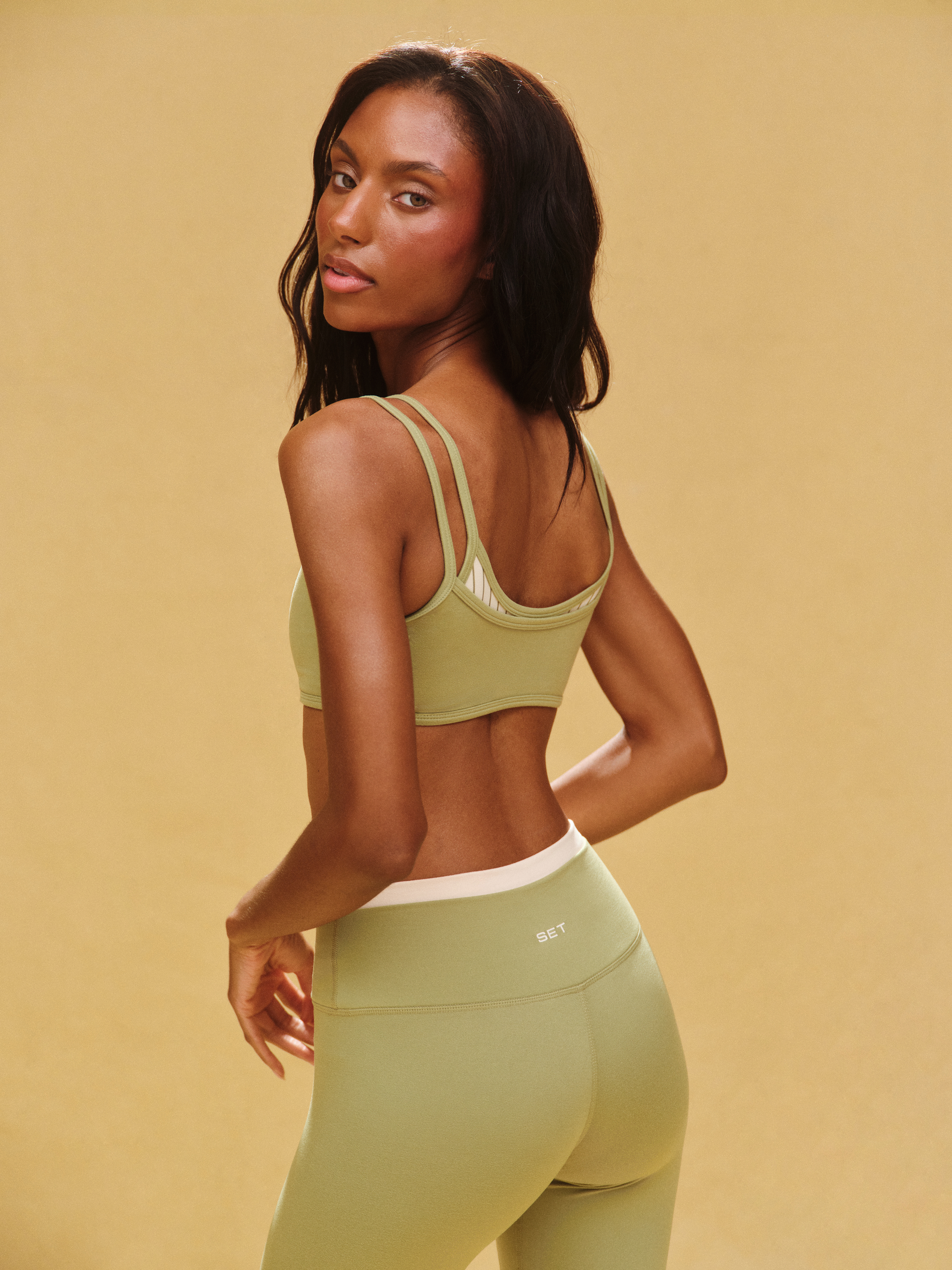 Woman wearing a green sports bra and leggings on a beige background