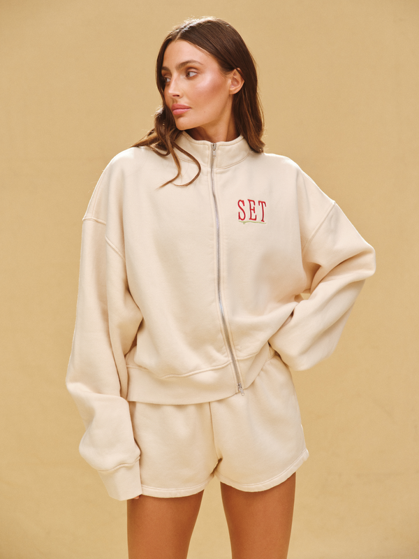 Woman wearing a beige tracksuit with 'SET' logo on a beige background 