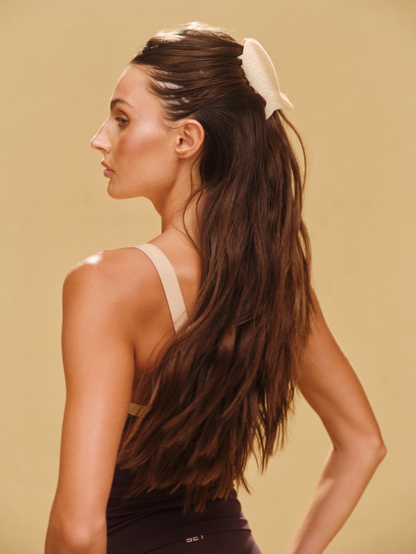Woman with long hair styled in a high ponytail against a beige background