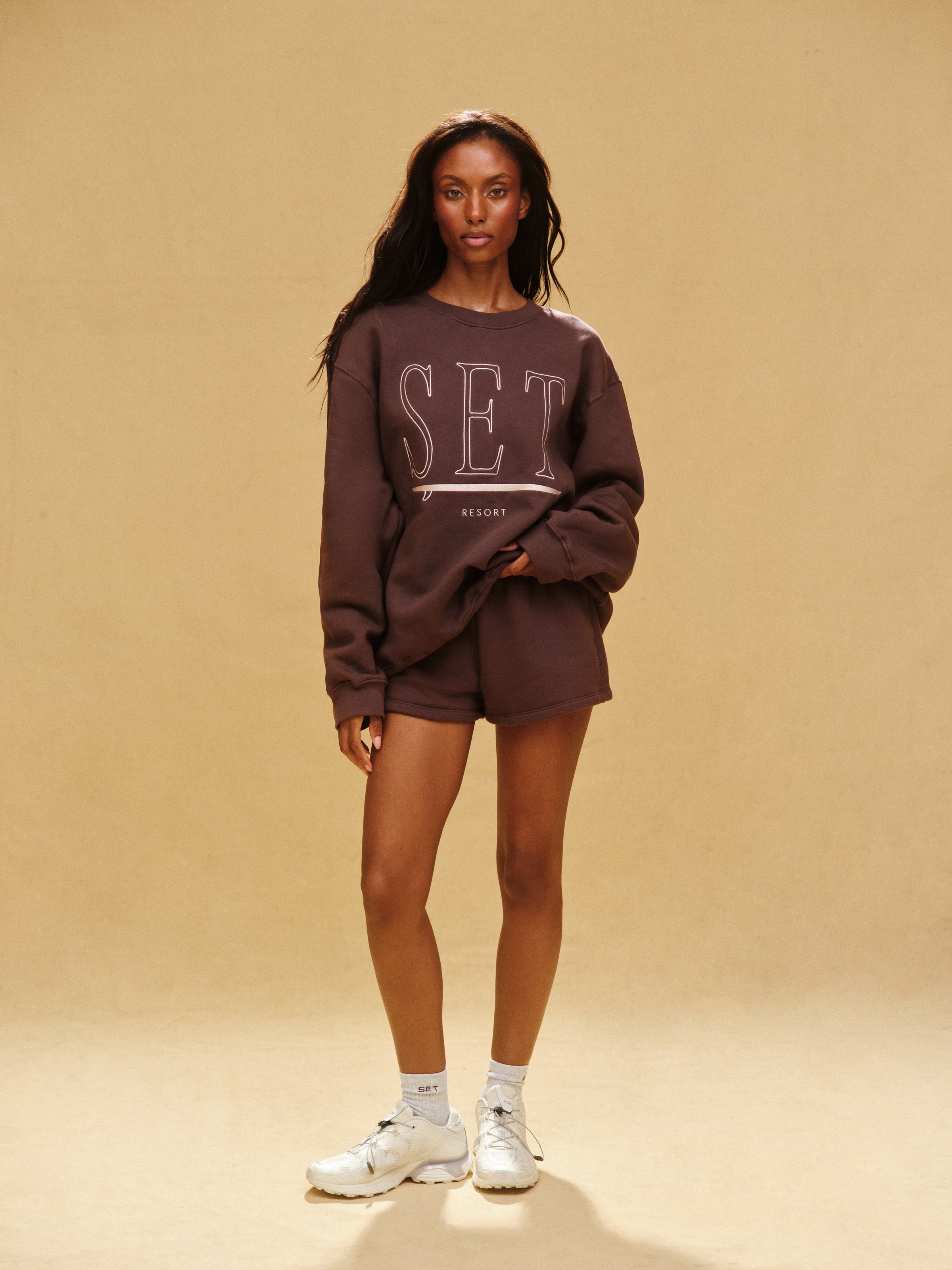 Person wearing a brown 'SET' sweatshirt and shorts on a beige background