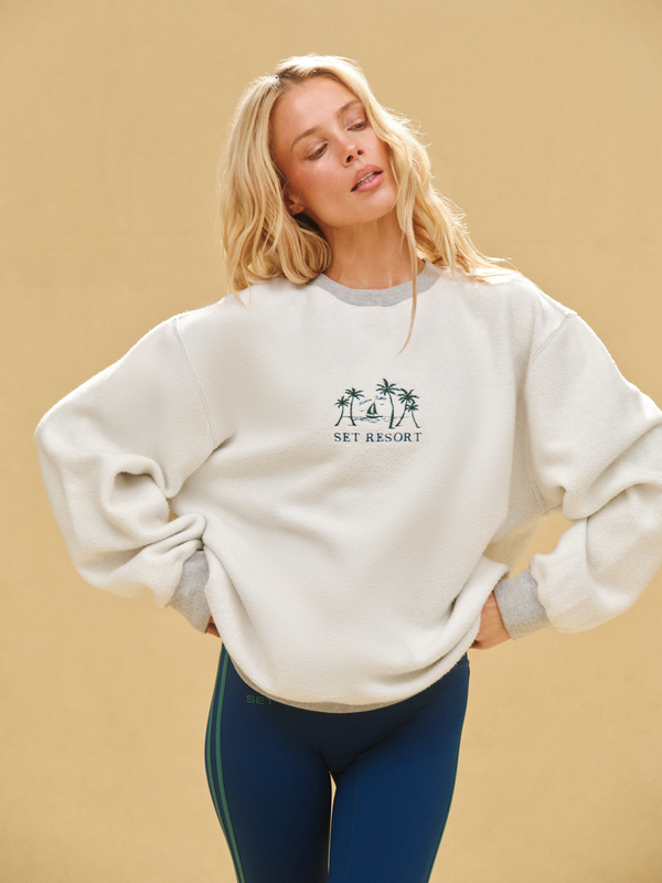 Woman wearing a white sweatshirt with a logo on a beige background 