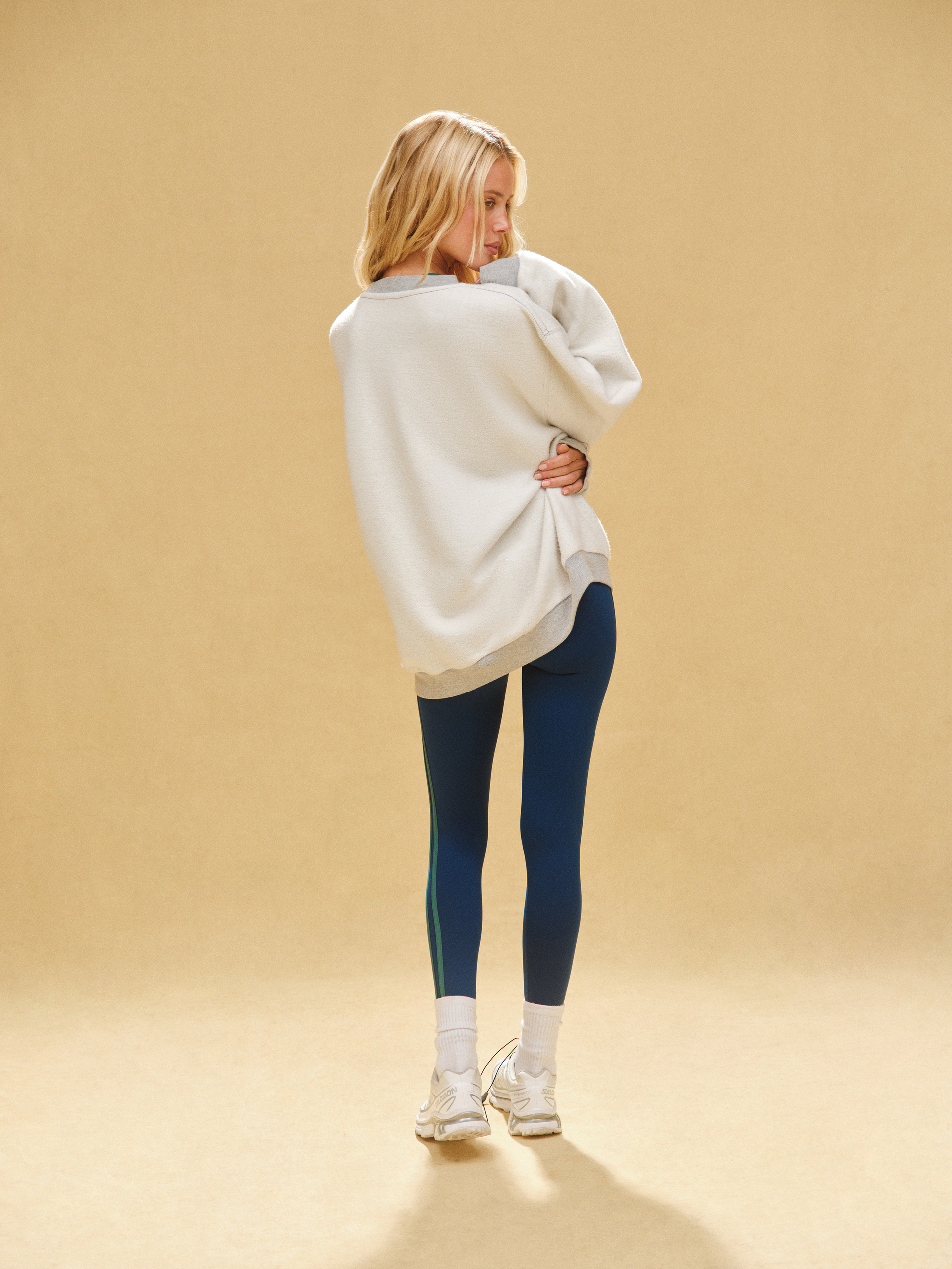 Person wearing a white oversized sweater and blue leggings on a beige background