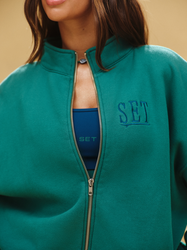 Teal jacket with 'SET' branding on a beige background