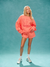 Person wearing a coral sweatshirt and shorts set with 'SET' branding on a teal background