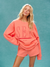 Woman wearing a coral sweatshirt with 'SET' text on a teal background <model-info>Allie wears a size M/L and is 5’7½, 25” waist, 32B bust.</model-info> 