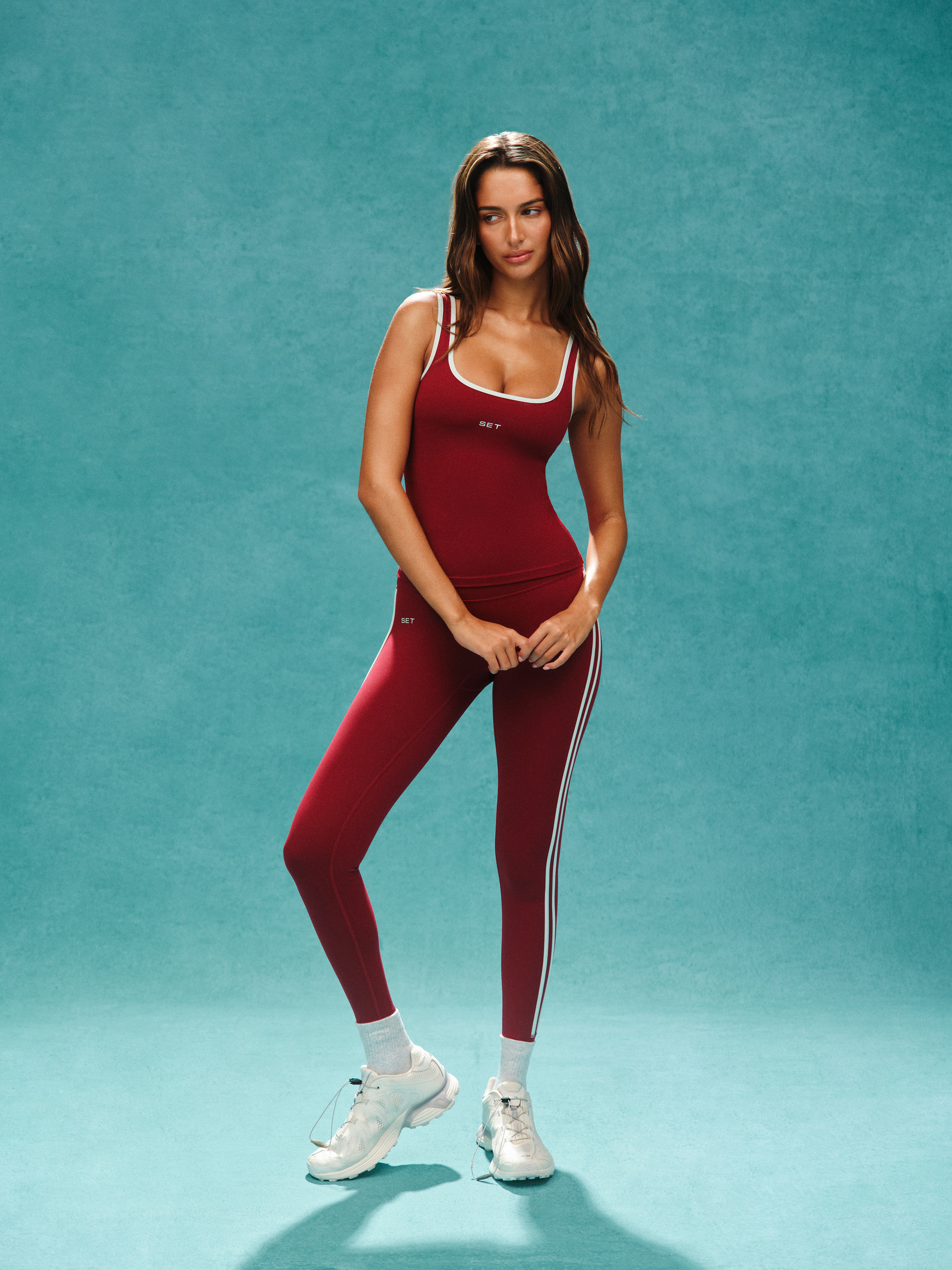 Woman wearing a maroon athletic outfit with white accents on a teal background