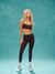 Woman wearing a dark sports bra and leggings on a teal background <model-info>Allie wears a size XS and is 5’7½, 25” waist, 32B bust.</model-info> 