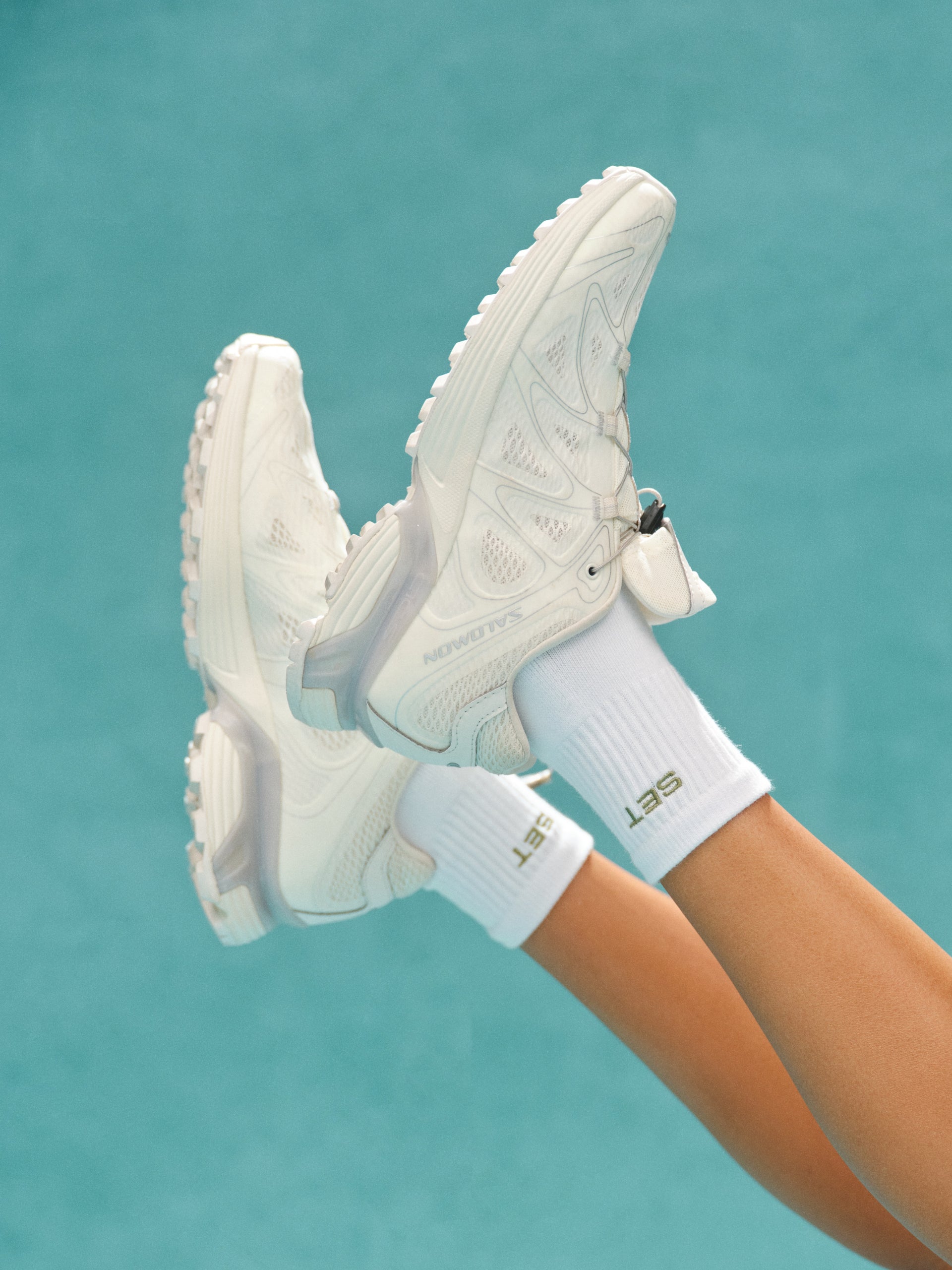 White sneakers and socks with a visible brand logo against a teal background