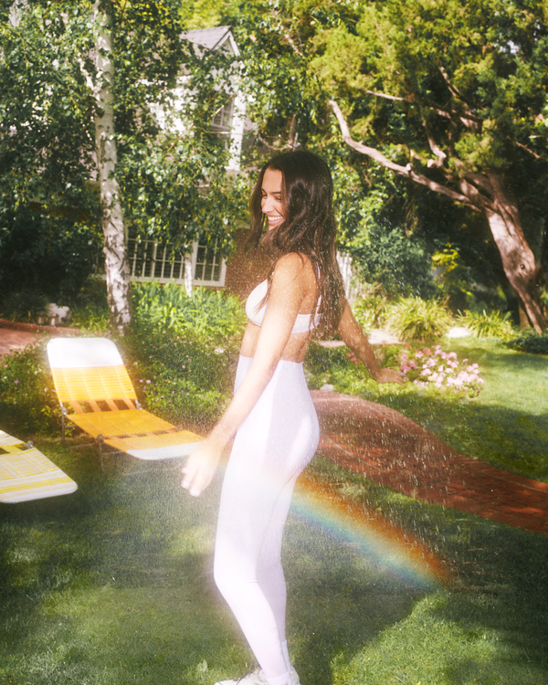 Woman in a white outfit standing in a garden with a rainbow effect