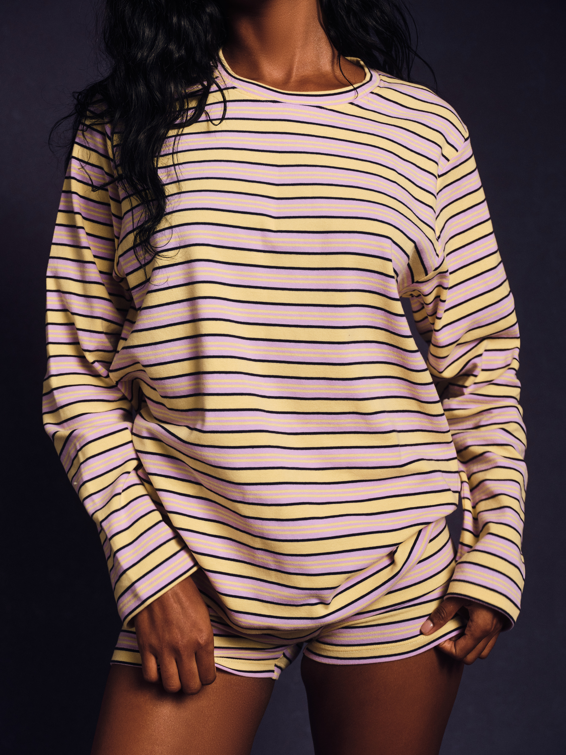 Person wearing a yellow and purple striped long-sleeve top and shorts on a dark background