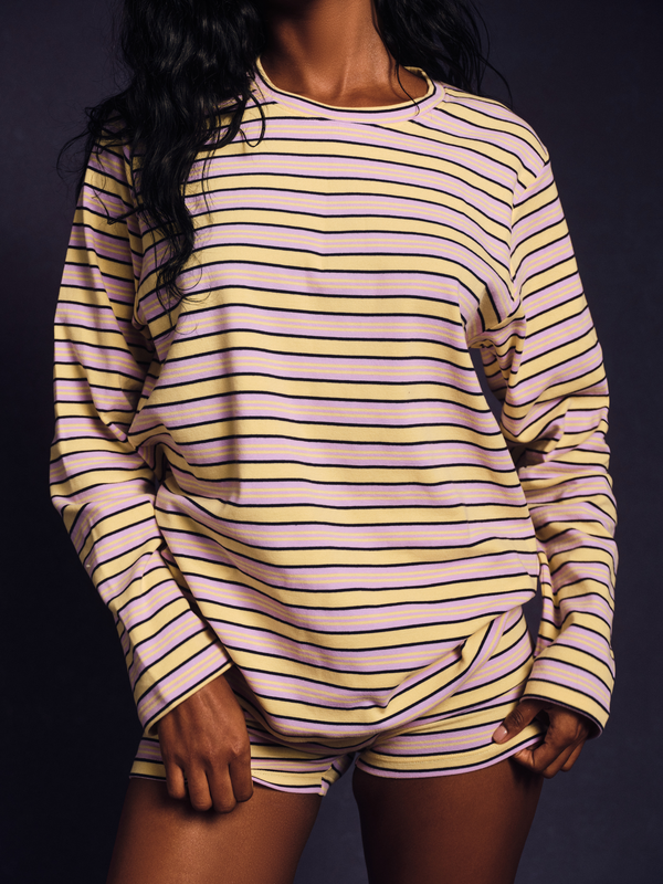 Person wearing a yellow and purple striped long-sleeve top and shorts on a dark background