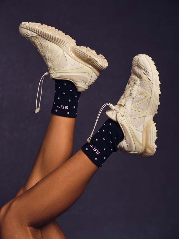 Person wearing white shoes with navy socks with pink polka dot detail.
