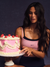 Woman holding a pink cake with cherries against a dark background
