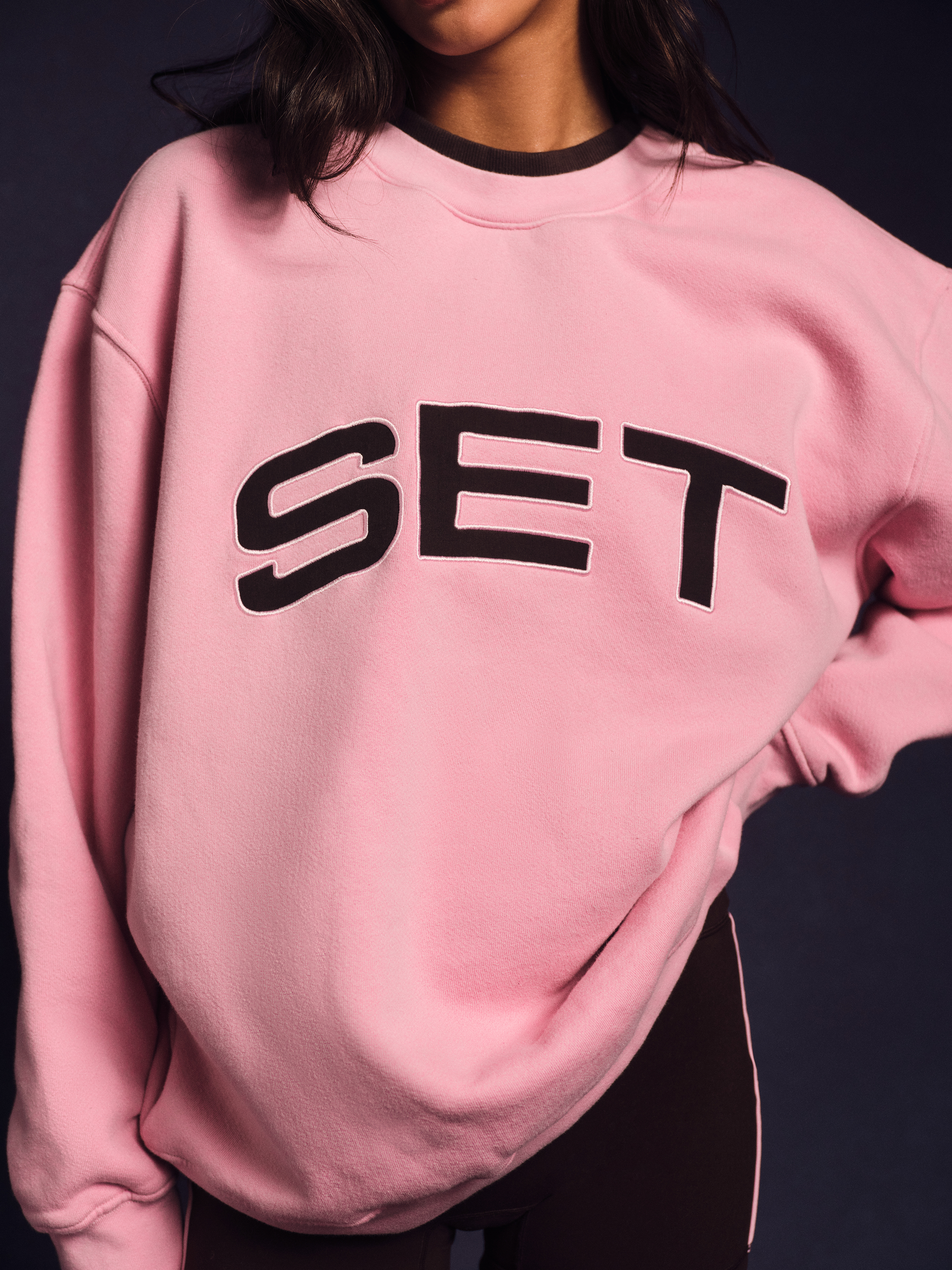 Person wearing a pink sweatshirt with 'SET' printed on it against a dark background