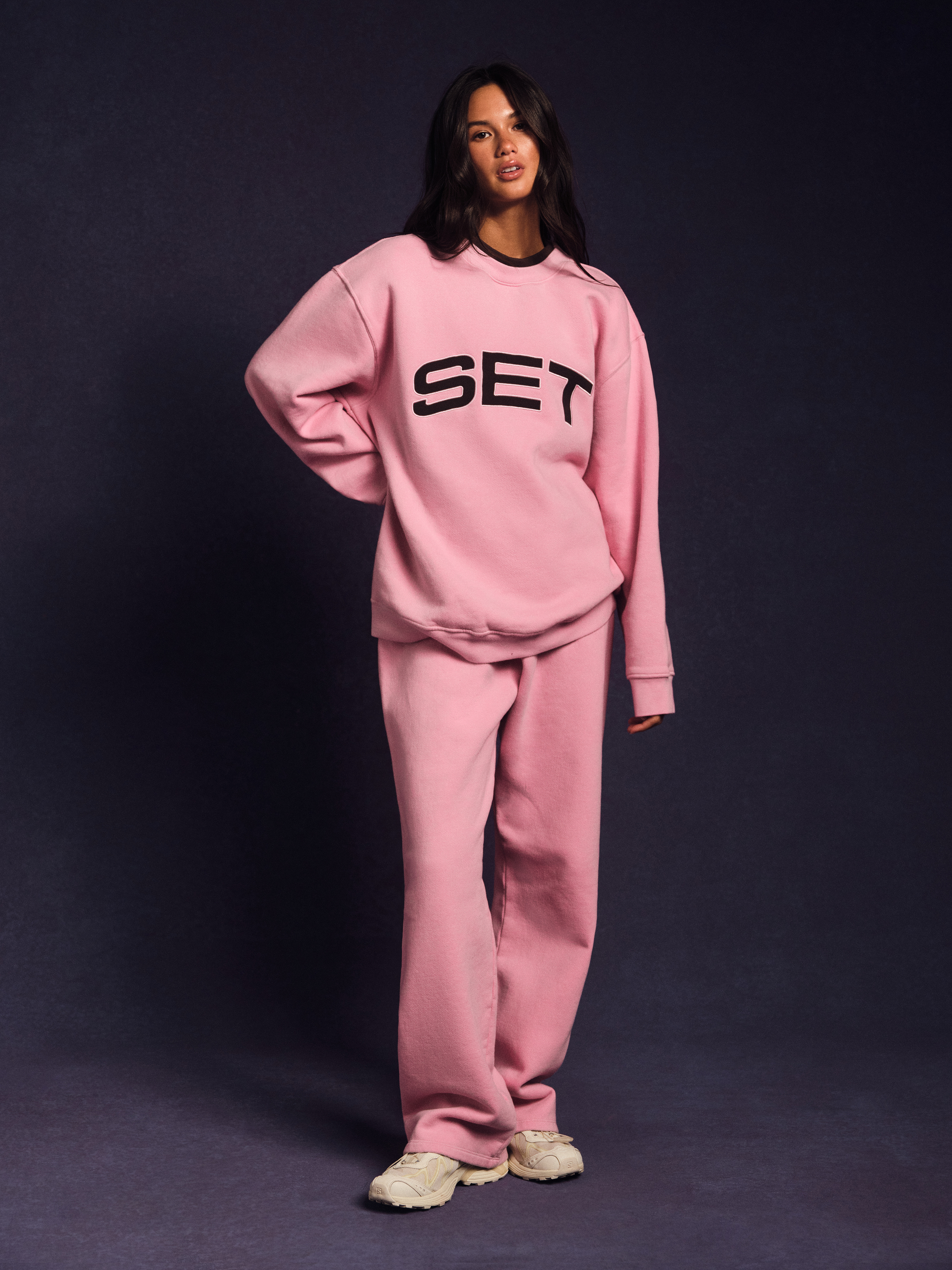 Person wearing a pink 'SET' tracksuit on a dark background  