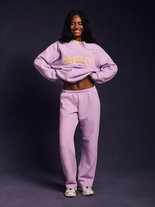 Person wearing a light purple 'GET' sweatshirt and pants on a dark background 