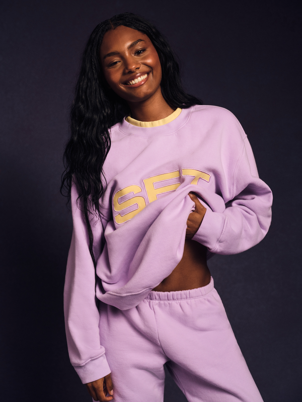 Woman wearing a purple sweatshirt with 'SET' logo on a dark background 